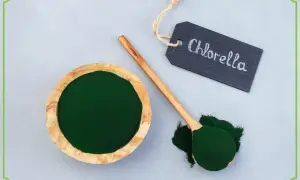 Zielony proszek w drewnianej miseczce i na łyżce. Tabliczka z napisem "Chlorella" wyjaśnia, co to jest chlorella.