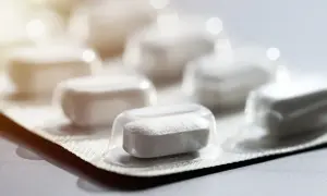 Białe tabletki w blistrze, jedna z nich wysunięta do przodu. Skudexa na kręgosłup, nadzieja na ulgę w bólu.