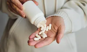 Ręka wysypuje białe kapsułki z pojemnika. Zastanawiasz się, gaba na co? To suplement diety.