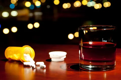 Szklanka z alkoholem i rozsypane tabletki paracetamolu na drewnianym blacie.