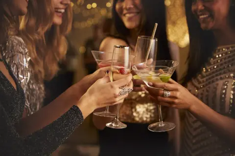 Kobiety w eleganckich strojach wznoszą toasty drinkami. Czy to czas na świętowanie, czy może na rozmowę o lekach jak metypred i alkohol?