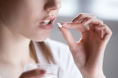 Kobieta bierze tabletkę clindamycin mip 600. Pije wodę, unikając alkoholu podczas leczenia.