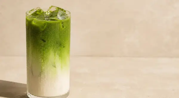 Orzeźwiająca matcha do picia z lodem w szklance, z widocznym podziałem na mleko i zielony napój.
