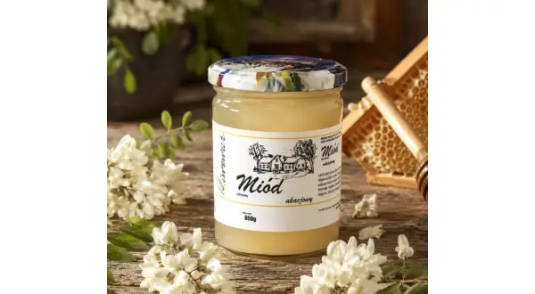 Słoik miodu akacjowego na drewnianym stole, otoczony kwiatami akacji. Miód akacjowy właściwości: delikatny smak, idealny do herbaty.