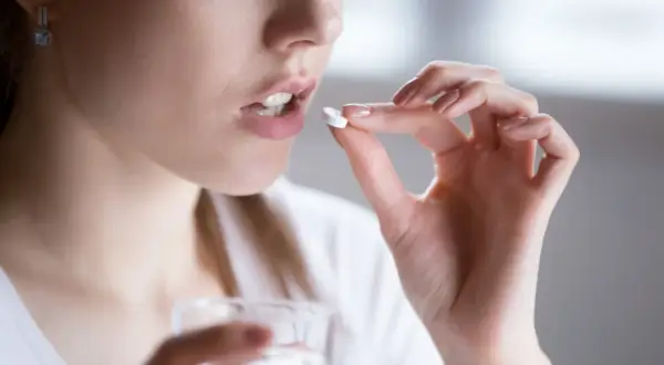 Kobieta bierze tabletkę clindamycin mip 600. Pije wodę, unikając alkoholu podczas leczenia.