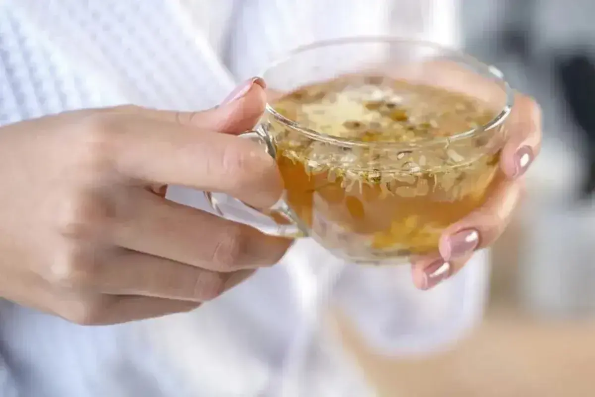 Dłonie trzymają szklankę z naparem z rumianku. Czy rumianek obniża ciśnienie? Napar wygląda na rozgrzewający i kojący.