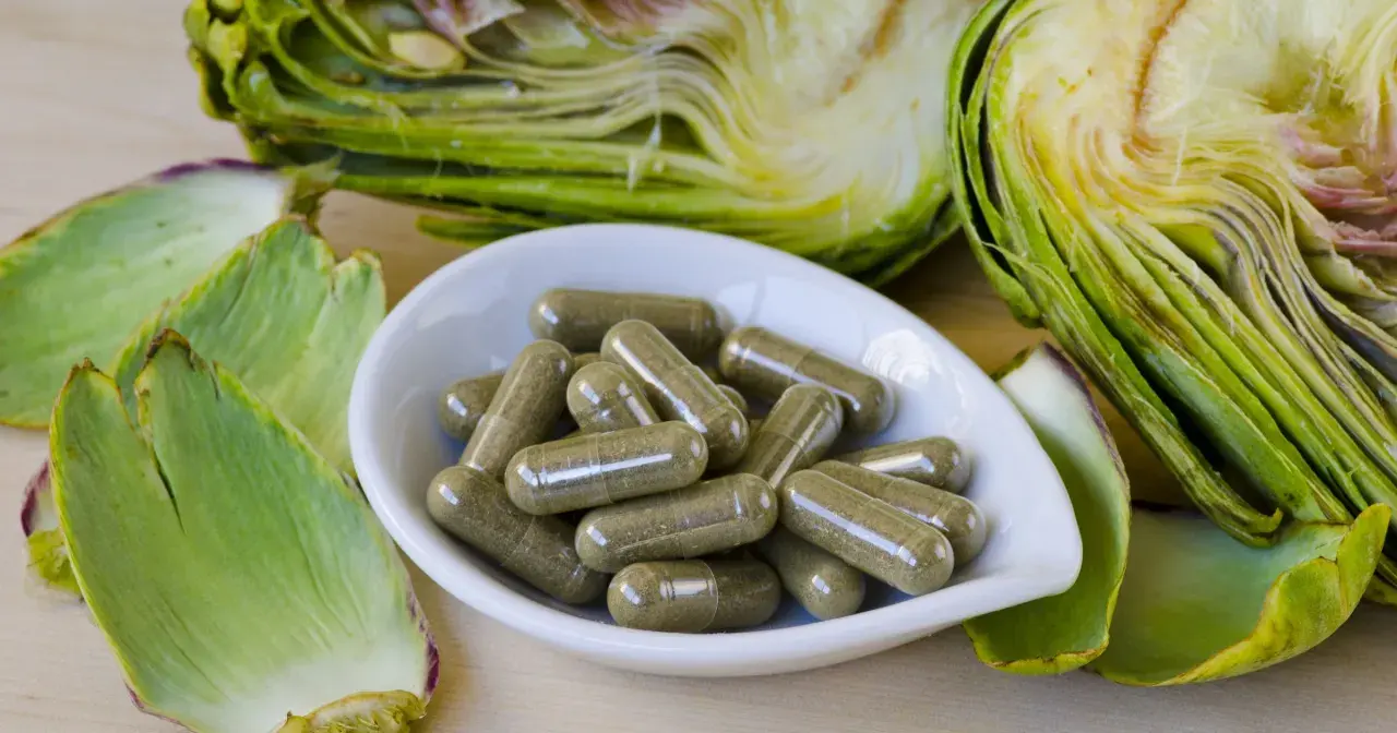 Karczochy co to? Świeże warzywa i kapsułki z ekstraktem z karczocha na drewnianym tle.