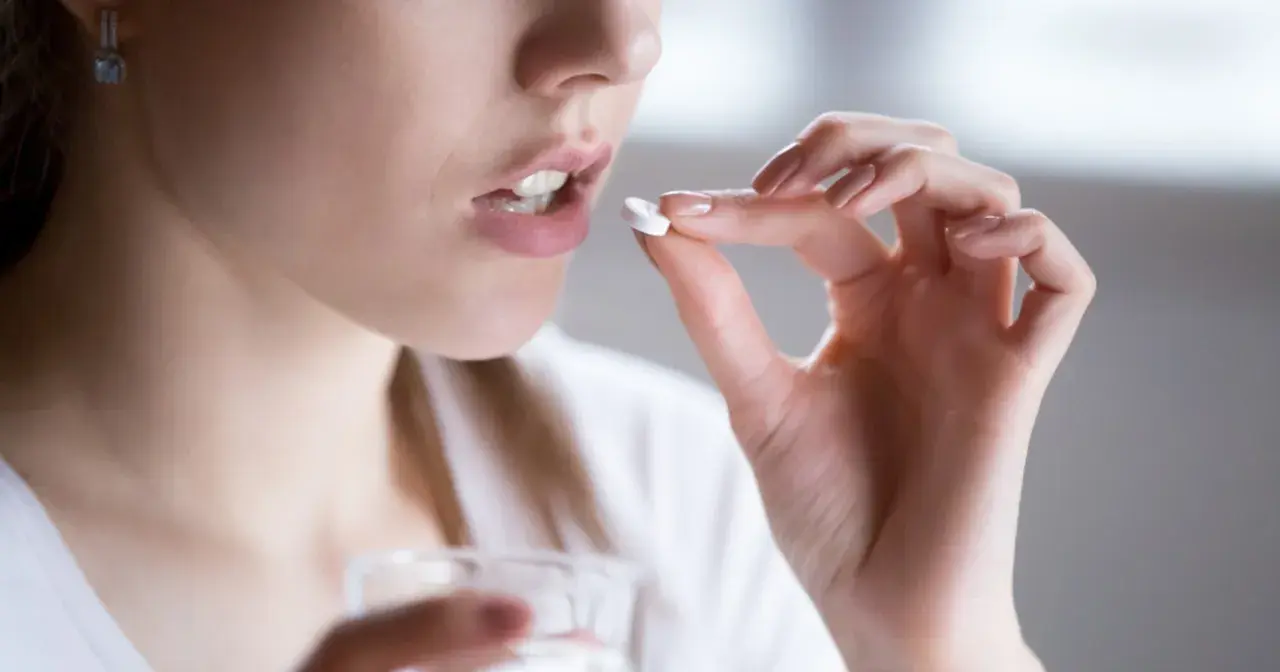 Kobieta bierze tabletkę clindamycin mip 600. Pije wodę, unikając alkoholu podczas leczenia.