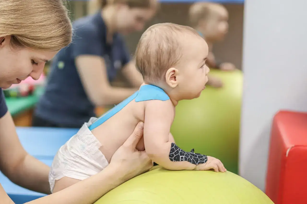 dziecko na rehabilitacji, fizjoterapia niemowląt, dziecko ćwiczy z fizjoterapeutą