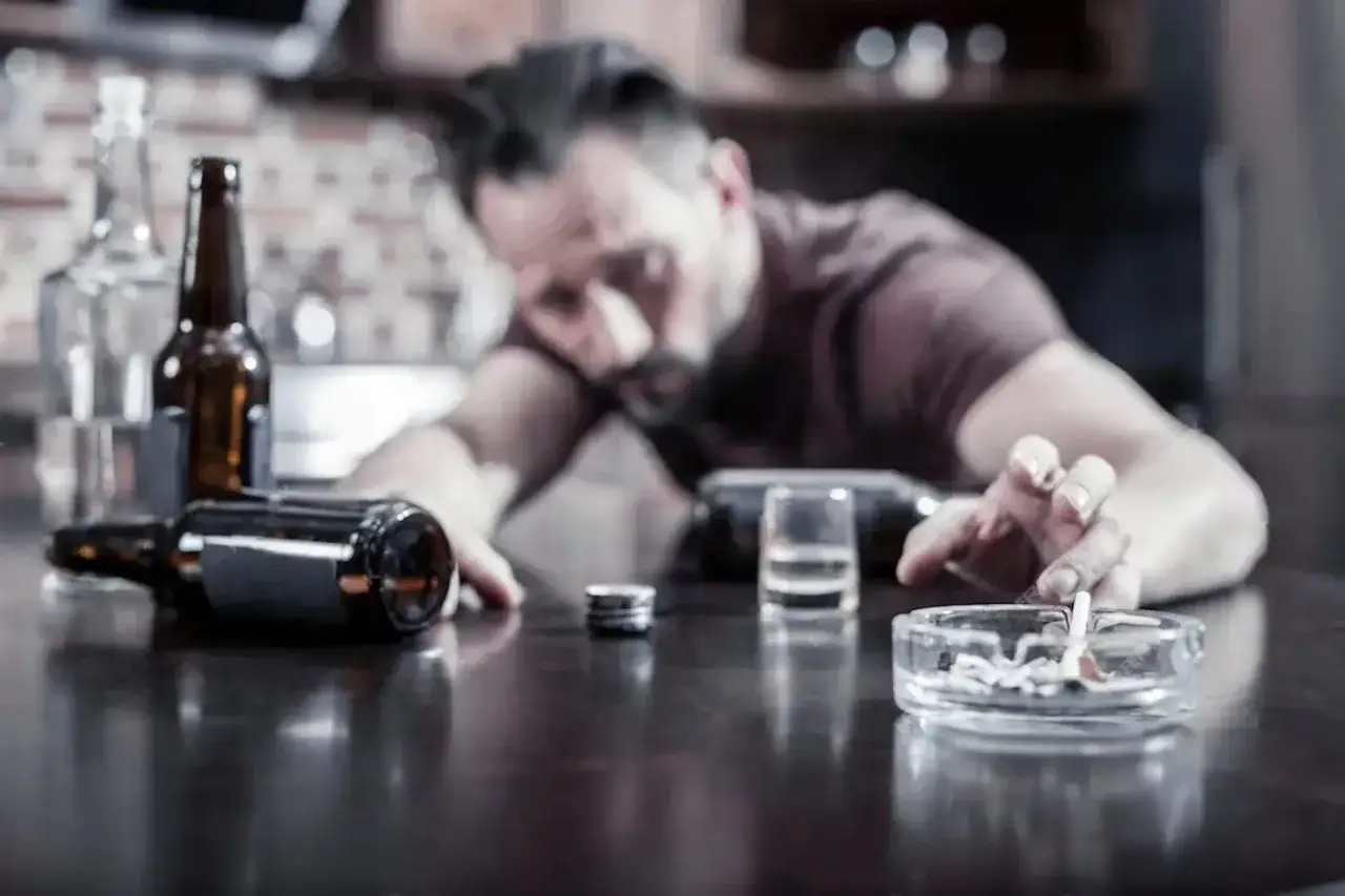 Mężczyzna w stanie upojenia alkoholowego, obok butelki i popielniczki z niedopałkiem. Clindamycin Mip 600 a alkohol to niebezpieczne połączenie.
